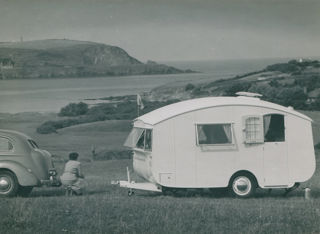 A Winchester Pipit caravan at a coastal location with a woman sat next to it