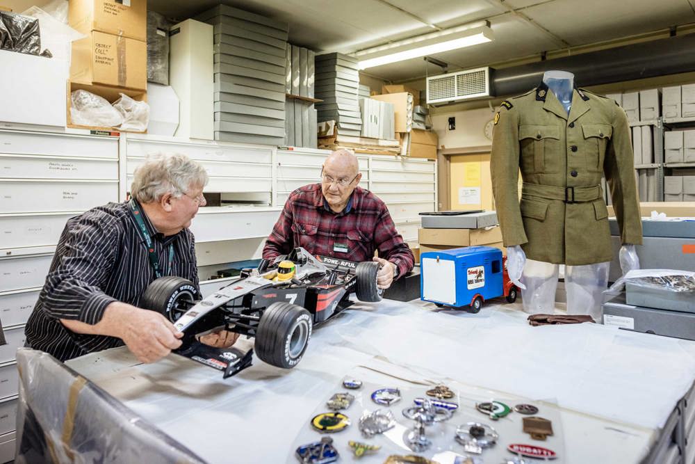 two male volunteers with formula one car model in objects store