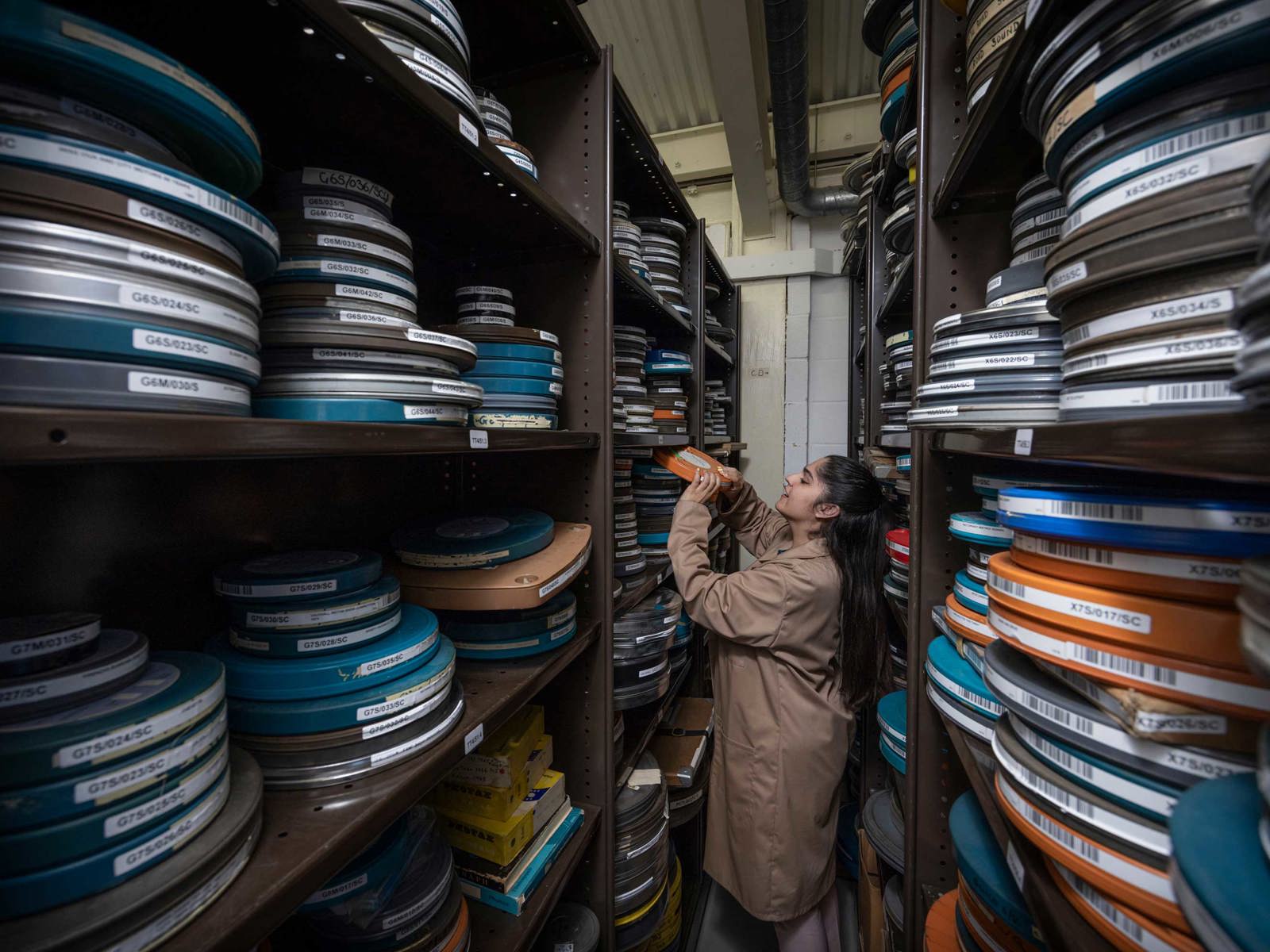 female member of staff in film stores removing film can from shelving