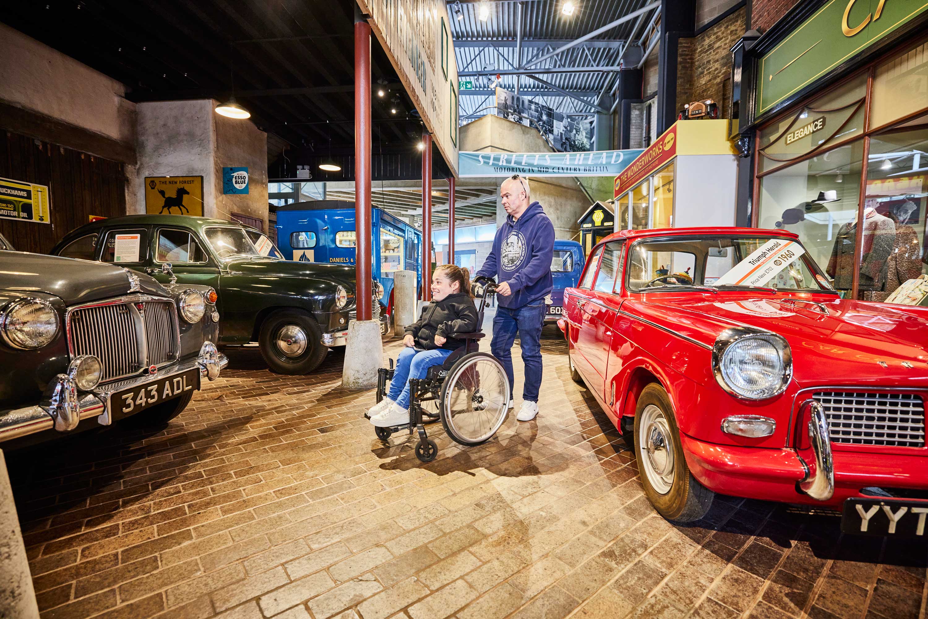 Male visitor with female wheelchair user in the Streets Ahead gallery in the National Motor Museum
