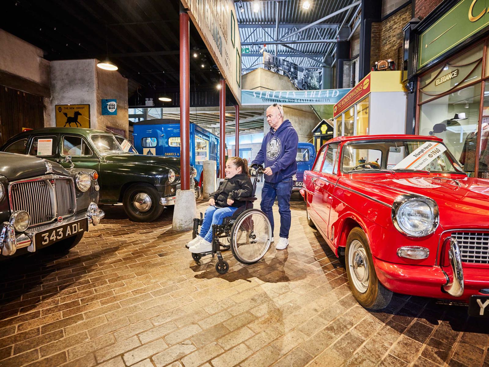 Male visitor with female wheelchair user in the Streets Ahead gallery in the National Motor Museum