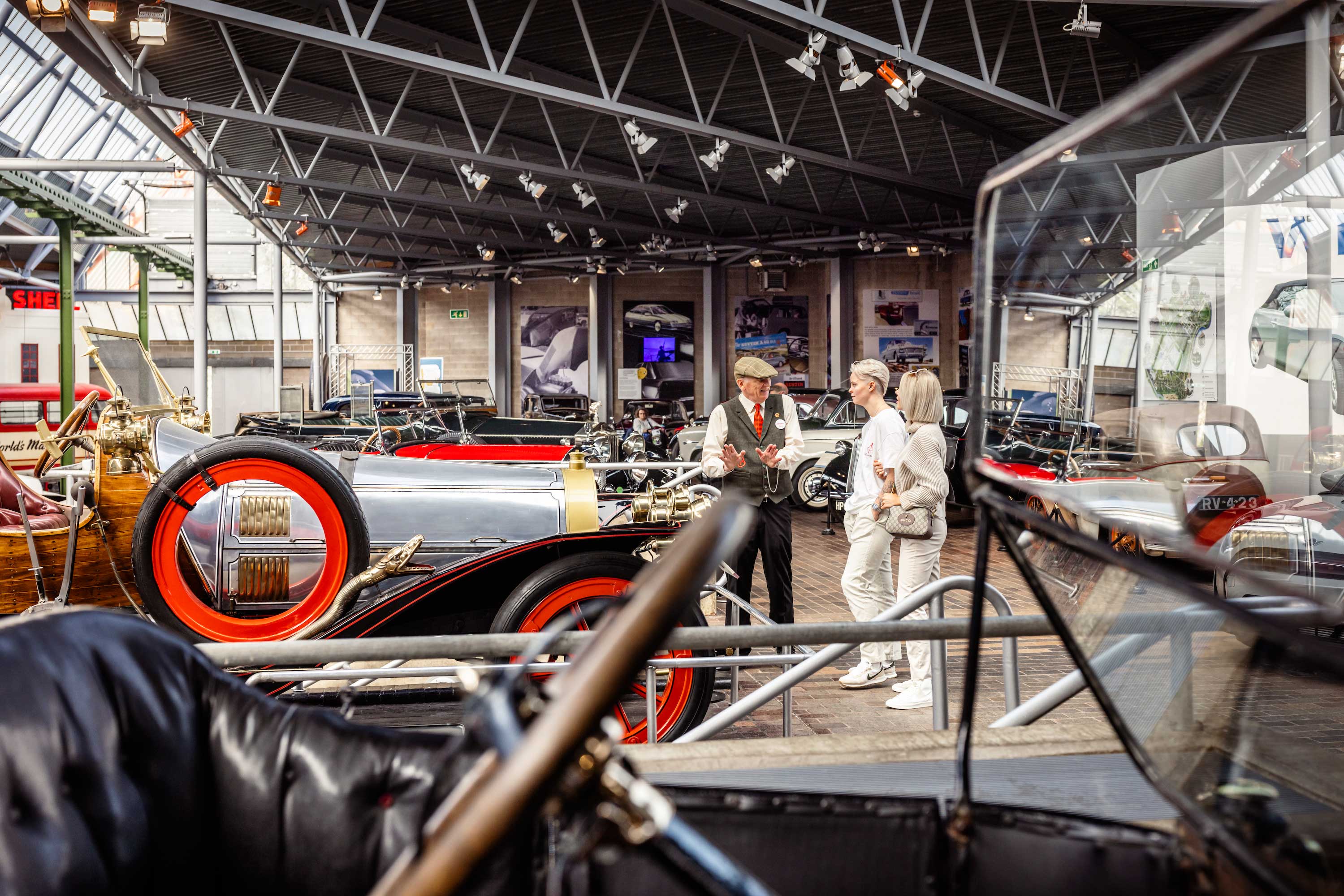 Two female visitors speak to a member of staff in the National Motor Museum