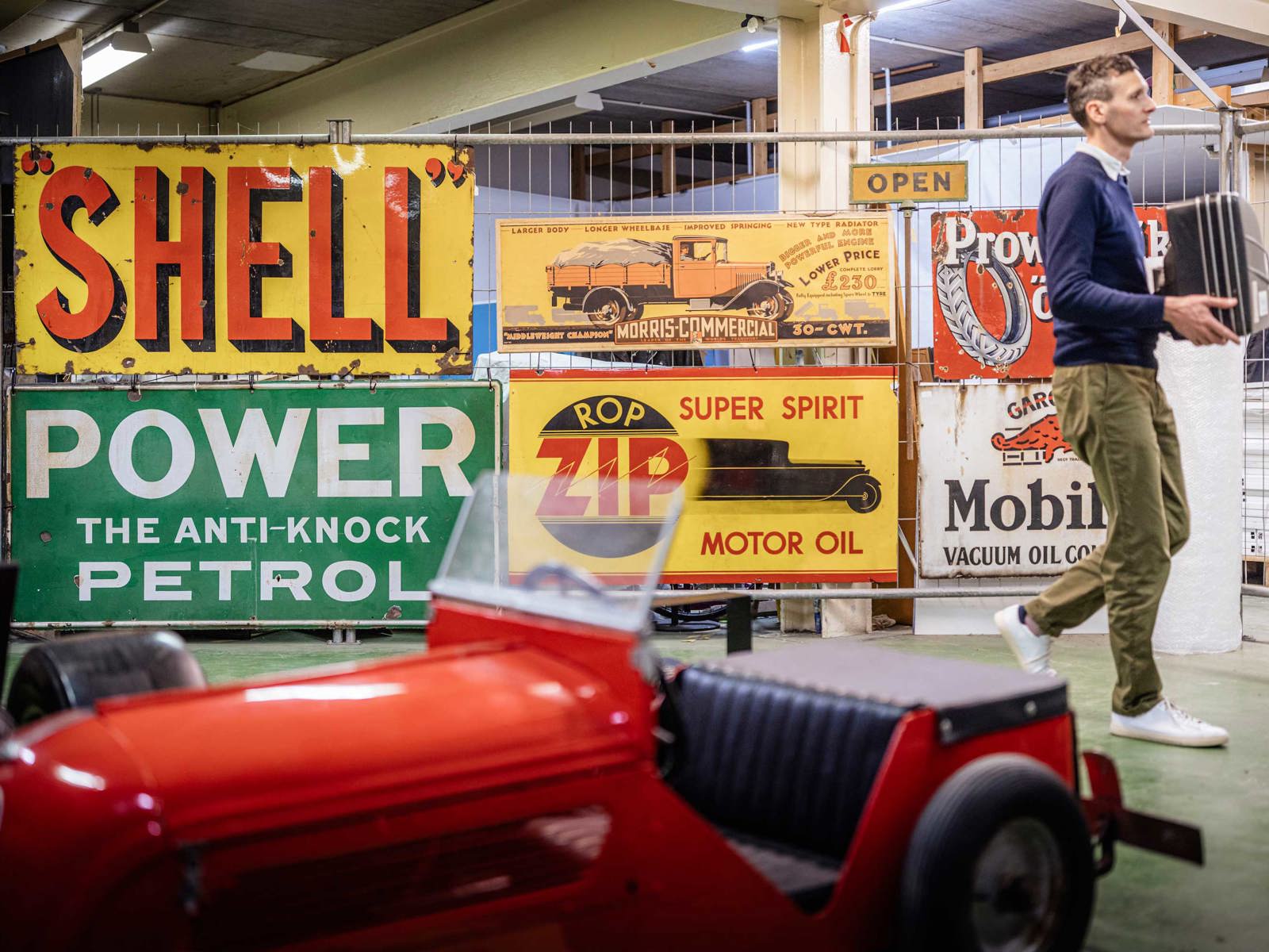 male member of staff carrying an object in front of a display of vintage metal advertising signs