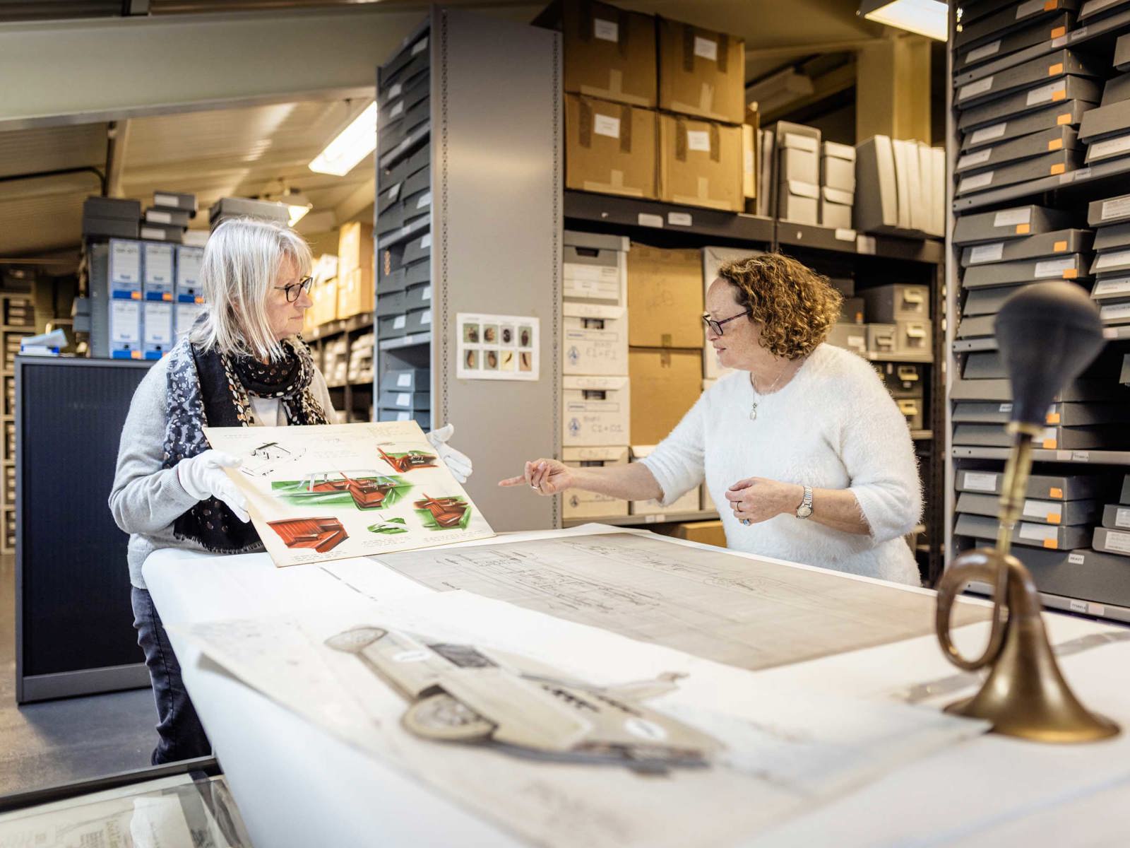 female curator holding up archive material for colleague to view in the archive store