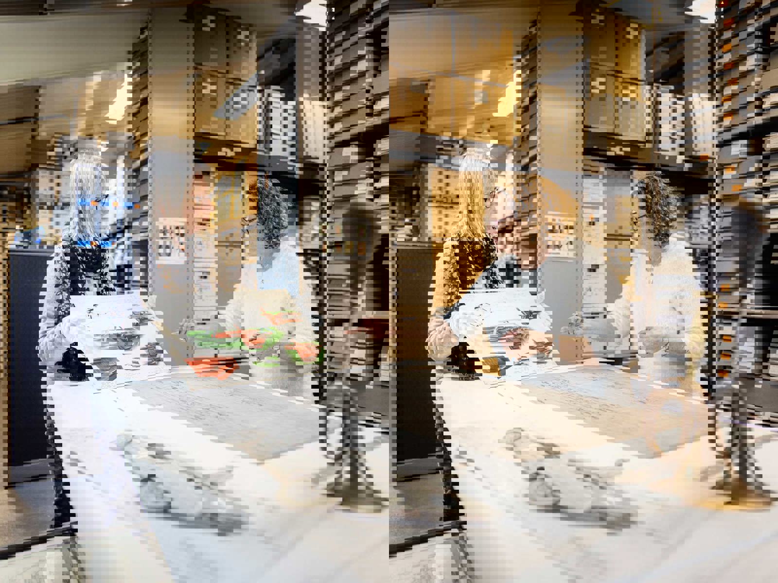 female curator holding up archive material for colleague to view in the archive store