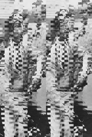 Raymond Mays leaning against racing car smoking