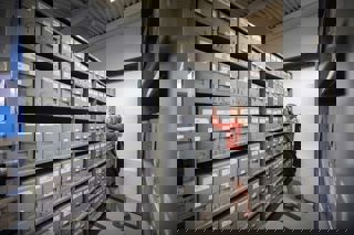 Female member of staff in the library store placing archive box on shelf