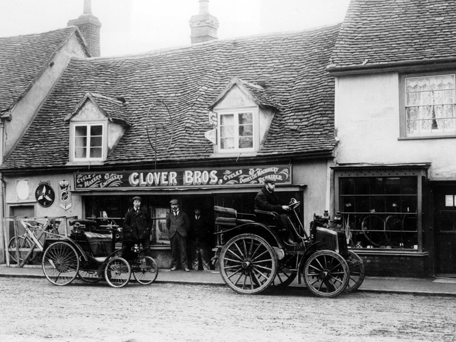 An archive image of a 1898 Benz and an early Panhard,, c1900, in a street outside Glover Bros cycle shop