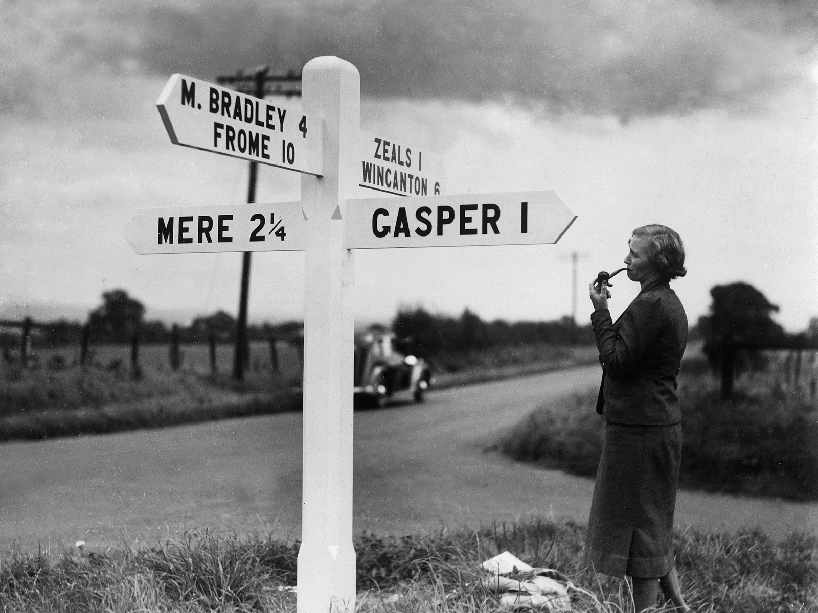 Archive image of lady at a crossroads looking at road sign c1930s