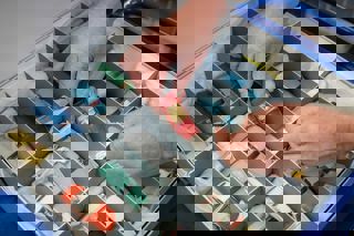 pair of hands holding a model car over an archive box of model cars