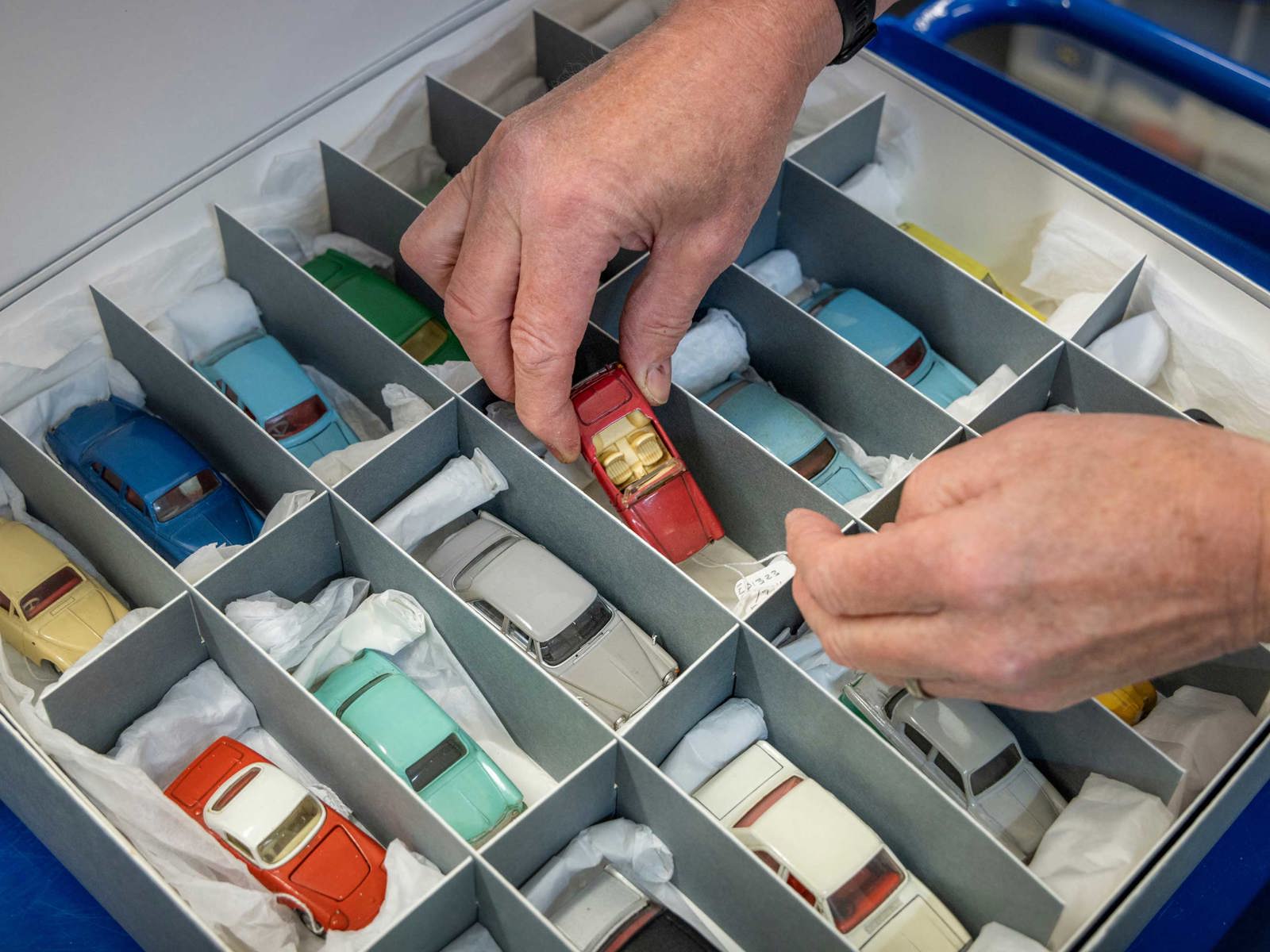 pair of hands holding a model car over an archive box of model cars