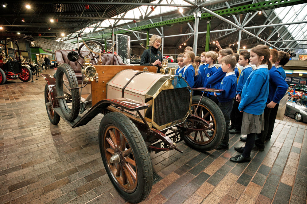 group of school children in the museum with education guide next to a 1909 Humber car