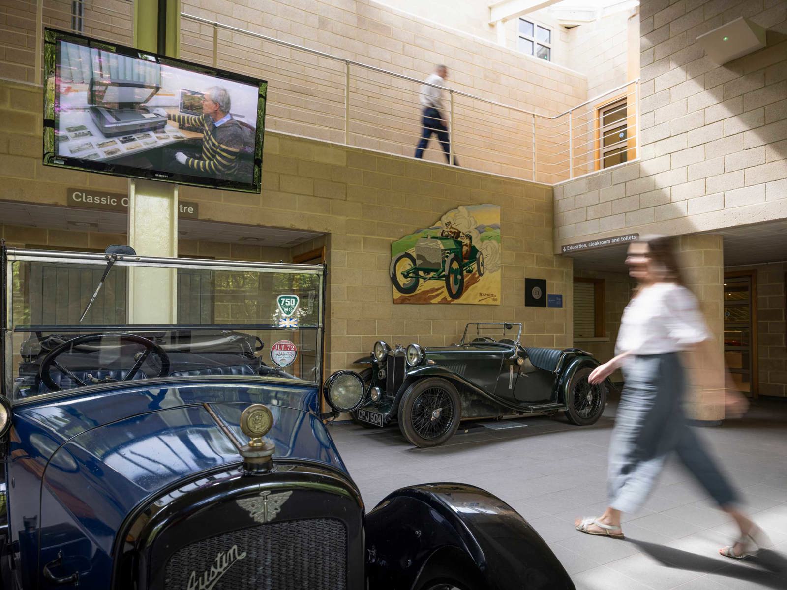 Collections Centre foyer with two historic vehicles on display and members of staff walking through